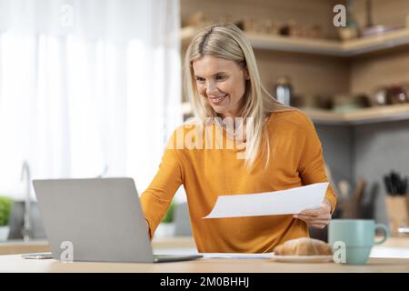 Attractive mature blonde woman freelancer working from home, reading documents Stock Photo