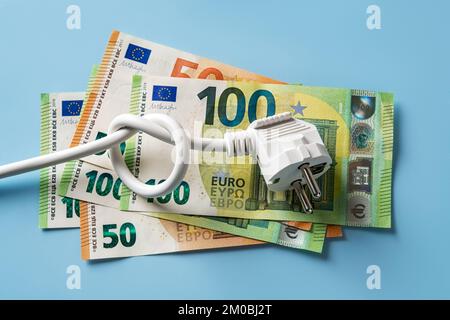 Knotted power cable with electric plug on 50 and 100 euro banknotes over blue background. Concept of rising energy costs in Europe. Energy price. Stock Photo