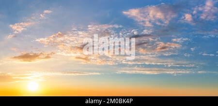 Settind sun low in the yellow blue evening sky. Light translucent orange clouds in the sunset heaven. Picturesque calm sundown skyscape. Idyllic vanil Stock Photo