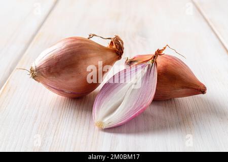Whole and half red eschalots on a white wooden table. Close-up of unpeeled long shallot bulbs. Fresh raw onion ready for cooking. Macro. Stock Photo