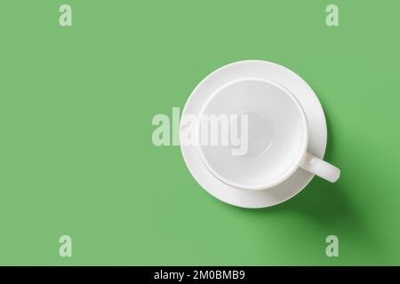 White mug over green background. Empty cup on a saucer closeup. Large teacup mockup for hot beverages design. Porcelain tableware and modern crockery. Stock Photo
