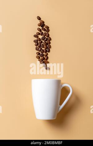 White mug and roasted coffee beans above it over beige background. Coffee drink and hot beverages concept. Large cup mockup for breakfast design. Stock Photo