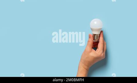 Light bulb in female fingers over blue background. Caucasian woman hand holding energy saving light bulb. Concept of education, how to do, explain. Stock Photo