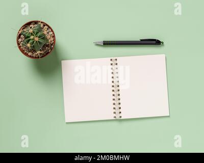 Blank notebook, pen and cactus over green background. Paper notepad for writing life goals, day organizing and business planning. Making to do list. Stock Photo