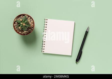 Empty notepad, pen and cactus against green background. Blank notebook for writing day planning, business organizing, life goals. Making to do list. Stock Photo