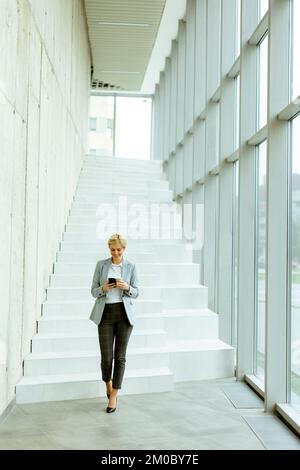 Businesswoman using mobile phone while walking on the modern office hallway Stock Photo