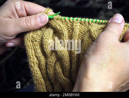 Person who knits a sweater with a braided pattern. Woman looking at her knitted sweater. Hand knitting. Stock Photo