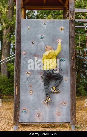 Boy At The Climbing Wall Without A Helmet, Danger At The Climbing Wall. Little Boy Climbing A Rock Wall Indoor Stock Photo