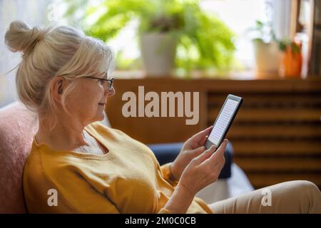 Senior woman using e-reader and reading an e-book at home Stock Photo