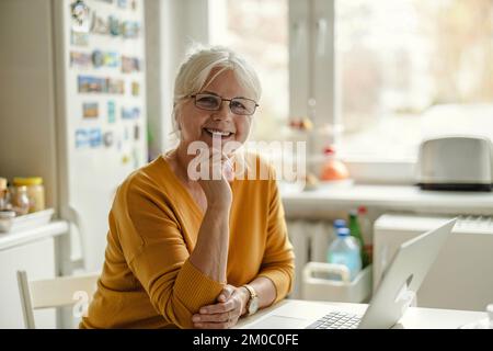 Mature woman working on laptop in kitchen Stock Photo