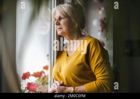 Worried elderly woman looking in window Stock Photo