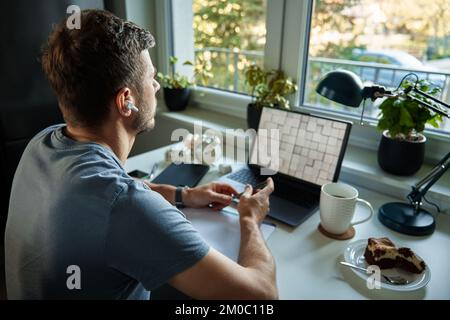 Freelancer working at home office. Man using laptop and writing in notepad sitting at table in home office Stock Photo