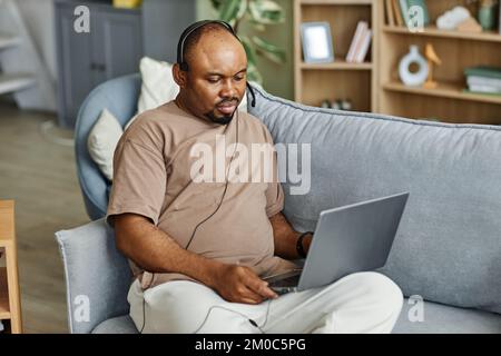 Portrait of black man using laptop with headset while working from home in online meeting, copy space Stock Photo