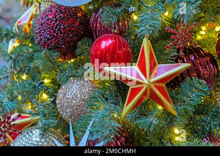 Five-pointed red star with a golden border on the Christmas tree with garlands. Stock Photo