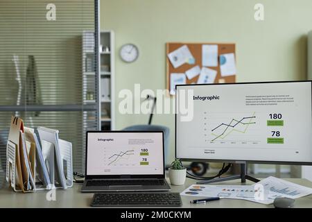 Background image of two computers with finance graphics and charts on screen at workplace in office setting Stock Photo