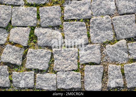 Texture of paved stone road with sprouted grass between masonry. Top view Stock Photo