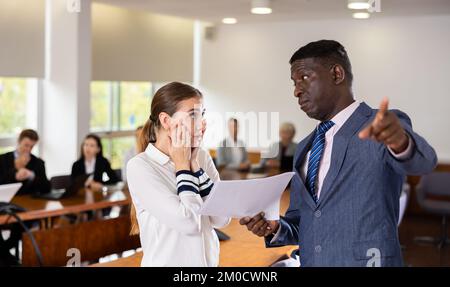 Middle aged african male boss being angry at young white female employee Stock Photo