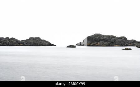 A minimalistic picture of dark rocks in the sea on a cloudy day, long exposure, vertical Stock Photo