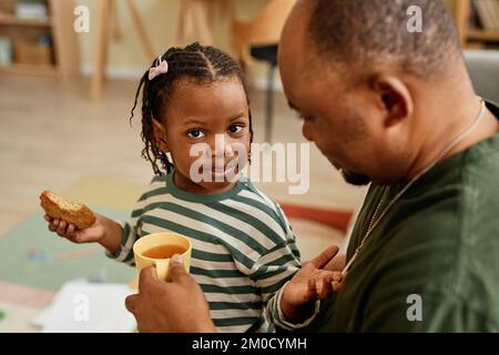 High angle portrait of cute black girl sharing cookies with father and looking at camera Stock Photo