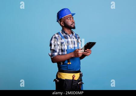 Portrait of African American contractor with digital tablet checking that all outstanding tasks on the agenda have been completed in interior renovation. Concentrated supervisor in studio shot. Stock Photo