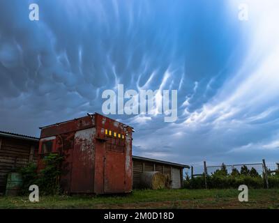 Red barn building container house before thunderstorm, dramatic sky with mammatus clouds Stock Photo