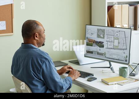 Side view portrait of black man as architect using computer and inspecting 3D blueprints Stock Photo