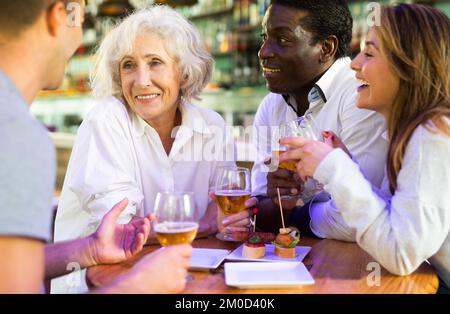 Cheerful family celebrating meeting or acquaintance with beer in bar. Focus on elderly woman Stock Photo