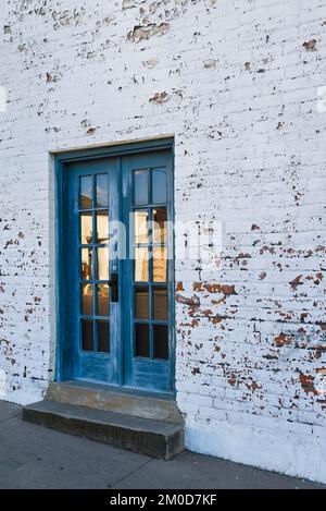 An aged &  blue patina on painted door with step to sidewalk in brick building with peeling, funky white painted brick wall in Tucson, AZ Stock Photo