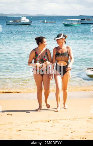 Mother and daughter, in bikinis, are coming out of the water at Porto da Barra beach in Salvador, Bahia. Stock Photo