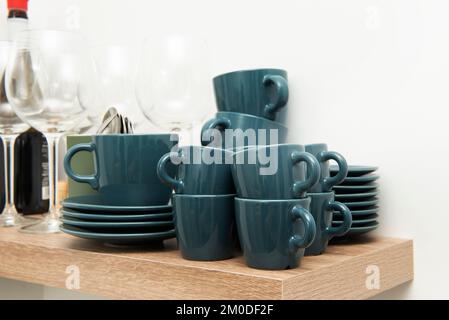 A blue colored china set with many matching saucers and cups alongside clear crystal wine glasses Stock Photo
