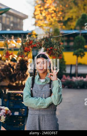 Farmer woman in denim overalls smiling sincerely showing okay sign. Stock Photo