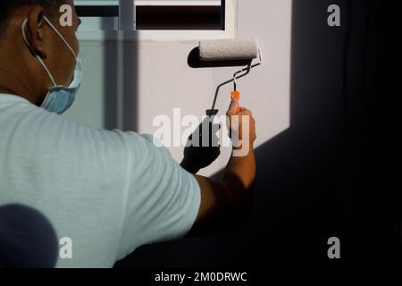 Male hand painting wall with paint roller. Painting wall room, renovating with grey color paint,The worker's hand paints the wall with a roller in gre Stock Photo