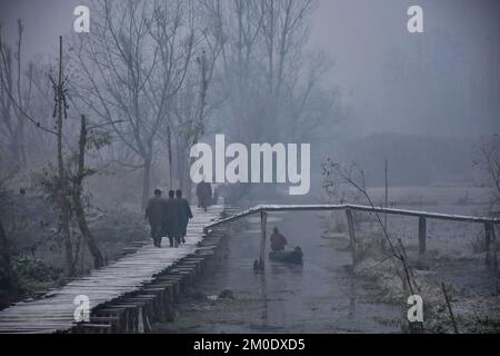 Srinagar, India. 05th Dec, 2022. Residents walk along a wooden foot-bridge in the interior of Dal lake during a cold foggy morning in Srinagar. Following the dip in temperatures, Kashmir is witnessing an intense cold wave and foggy weather conditions. The weatherman has forecast a two-day wet spell between December 9 and 10 in the region. Credit: SOPA Images Limited/Alamy Live News Stock Photo