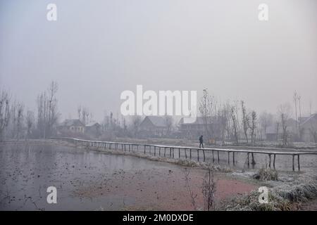 Srinagar, India. 05th Dec, 2022. A man walks along a wooden foot-bridge in the interior of Dal lake during a cold foggy morning in Srinagar. Following the dip in temperatures, Kashmir is witnessing an intense cold wave and foggy weather conditions. The weatherman has forecast a two-day wet spell between December 9 and 10 in the region. Credit: SOPA Images Limited/Alamy Live News Stock Photo