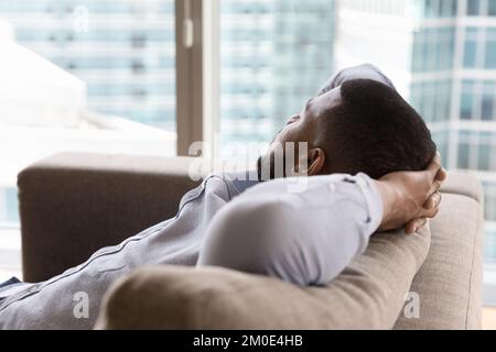 Dreamy sleepy young Black man relaxing on couch Stock Photo
