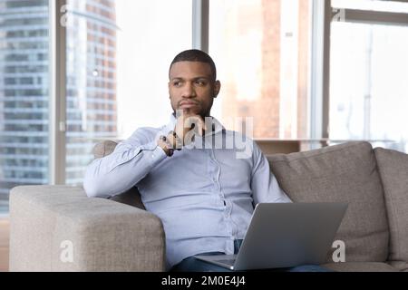 Pensive thoughtful African freelance business man holding laptop on lap Stock Photo