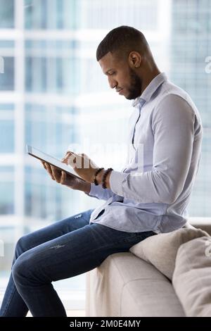 Serious handsome young millennial freelancer man using tablet Stock Photo