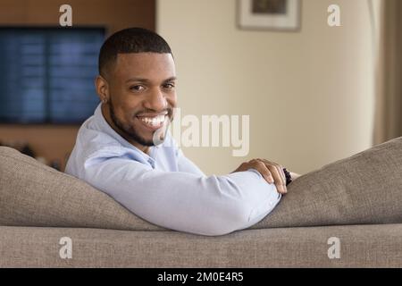 Happy handsome young Black homeowner man sitting on couch Stock Photo