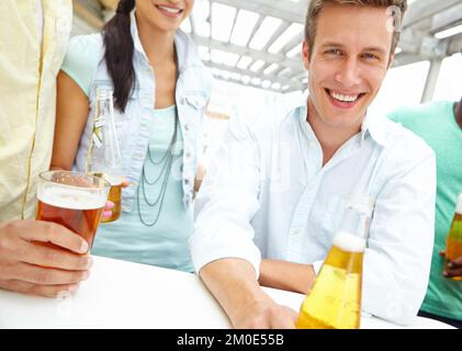 He enjoys a beer or two. Portrait of a handsome young man enjoying drinks on the outdoors deck of a restaurant. Stock Photo