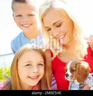 We love our puppy. a mother with her two children playing with a puppy outside. Stock Photo