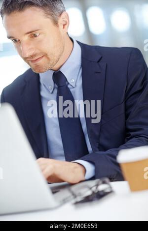 Focused on the job at hand. Handsome mature businessman using his laptop while seated at his desk. Stock Photo