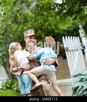 Daddys home. An army father at home in the garden hugging his two children. Stock Photo