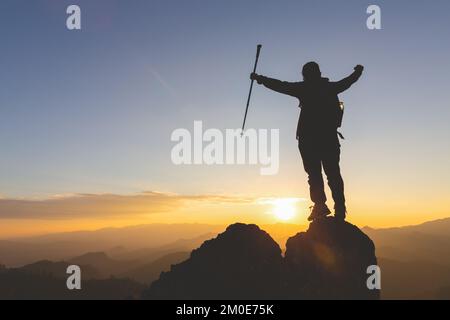 Silhouette of young woman standing alone on top of mountain and raise both arms praying and  enjoying nature,   Demonstrates hope and freedom, success Stock Photo