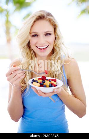 Delicious choice. Portrait of a pretty yong woman smiling while eating a fruit salad. Stock Photo
