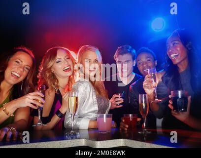 Enjoying the citys night spots. A multi-ethnic group of young friends smiling at the camera while they enjoy drinks in a nightclub. Stock Photo