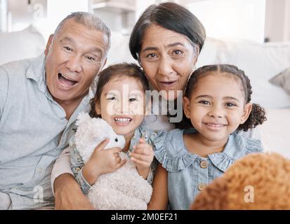 Closeup of to mixed race grandparents playing with their granddaughters and their teddy bears on the sofa at home. Family having a fun time at home Stock Photo