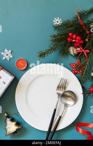 Flat lay of Christmas table setting with plate, cutlery, gifts boxs and christmas decorations on green background. Stock Photo