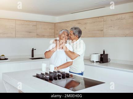 Mixed race senior couple hugging in the morning at home. Smiling elderly husband and wife holding each other and embracing in kitchen. Happy retired Stock Photo