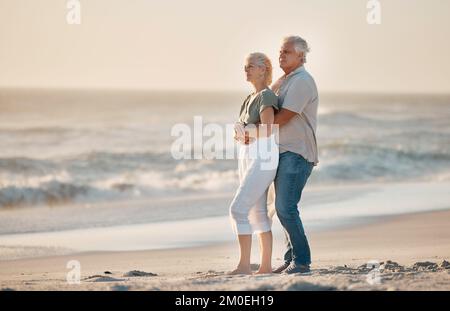 Mature husband hugging his wife on the beach. Senior couple being affectionate on the beach. Senior couple enjoying the view by the ocean. Mature Stock Photo