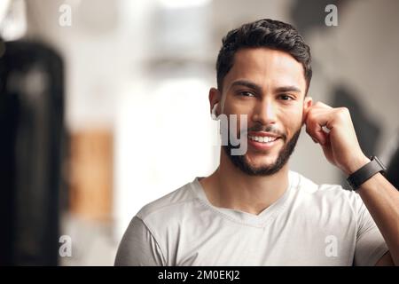 Portrait of one confident young hispanic man listening to music with wireless bluetooth earphones to stay motivated while exercising in a gym. Happy Stock Photo